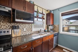 Kitchen featuring wood cabinetry, a mosaic tile backsplash, dark granite countertops, a stainless steel double basin sink, and an over-the-range microwave - 