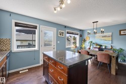 Kitchen and dining area featuring wood-finish flooring, a central island with a stone countertop and integrated storage, and a light blue wall color - 