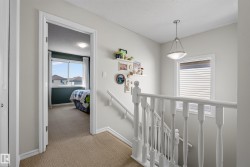Upper-level hallway featuring a carpeted floor, white painted balusters and handrail, a ceiling-mounted light fixture, and a window with horizontal blinds - 