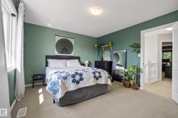 Carpeted bedroom featuring a window with white curtains, a neutral ceiling, and a doorway opening to a hallway with white banisters - 