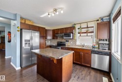 Kitchen featuring dark wood cabinetry, stainless steel appliances, a center island with a stone countertop, and wood-finish flooring - 