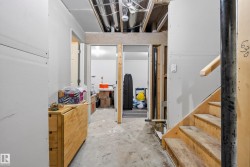 Unfinished basement space with exposed ceiling joists and ductwork, featuring a wood staircase with a natural wood handrail - 