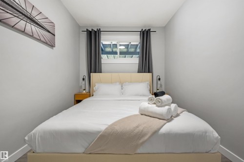 Bedroom featuring a light-toned upholstered headboard, a window with dark drapes, and wood-finish flooring - 4001 113 Avenue Nw, Edmonton, AB - Indoor Photo Showing Bedroom