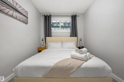 Bedroom featuring a light-toned upholstered headboard, a window with dark drapes, and wood-finish flooring - 