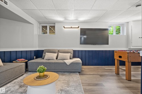 Finished basement featuring wood-finish flooring, two egress windows, a wall-mounted television, and a drop ceiling - 4001 113 Avenue Nw, Edmonton, AB - Indoor