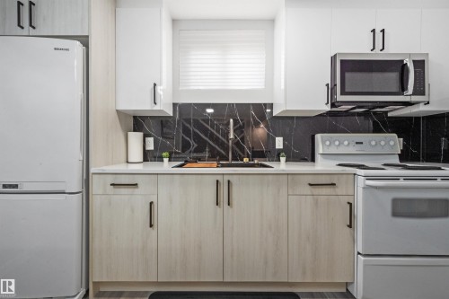 Modern kitchen featuring a black marble-look backsplash, light wood-finish lower cabinetry, white upper cabinetry, and light countertops - 4001 113 Avenue Nw, Edmonton, AB - Indoor Photo Showing Kitchen