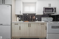 Modern kitchen featuring a black marble-look backsplash, light wood-finish lower cabinetry, white upper cabinetry, and light countertops - 