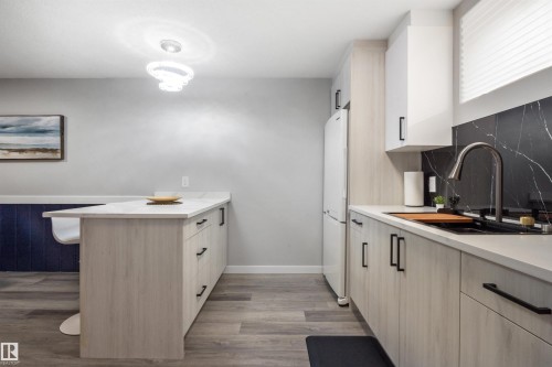 Modern kitchen featuring light wood-finish cabinetry with matte black hardware, stone countertops, and a black slab backsplash with white veining - 4001 113 Avenue Nw, Edmonton, AB - Indoor Photo Showing Kitchen