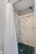 Shower enclosure featuring white marble-look wall tiles with dark veining and a green square tile floor - 