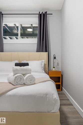 Contemporary bedroom featuring a beige upholstered headboard, a window with dark privacy curtains, and light gray walls - 4001 113 Avenue Nw, Edmonton, AB - Indoor Photo Showing Bedroom