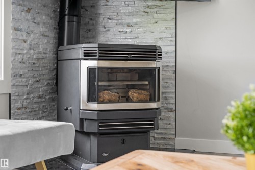 Contemporary wood-burning stove with a glass door, set against a stacked stone accent wall - 4001 113 Avenue Nw, Edmonton, AB - Indoor With Fireplace