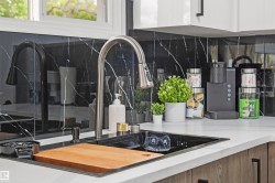 Integrated black sink with a wood cutting board, brushed steel gooseneck faucet, black marble-style backsplash, white countertops, and wood-finish lower cabinetry - 