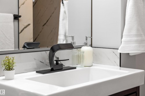 White rectangular sink with a matte black faucet, set against a marble-patterned backsplash and a frameless mirror - 4001 113 Avenue Nw, Edmonton, AB - Indoor