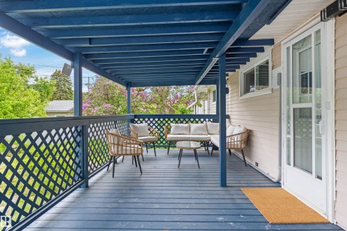 Spacious covered deck featuring blue-painted wood flooring, a lattice railing, and a beige exterior wall with a white-framed door - 4001 113 Avenue Nw, Edmonton, AB - Outdoor With Deck Patio Veranda With Exterior