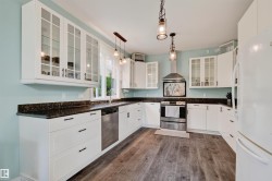 Kitchen featuring white cabinetry, dark speckled countertops, wood-finish flooring, stainless steel appliances, and pendant lighting - 