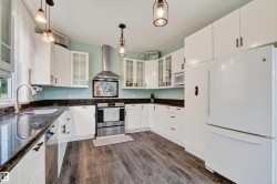 Kitchen featuring dark countertops, white cabinetry, stainless steel range with hood, and wood-finish flooring - 
