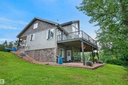Sloping green lawn surrounding a multi-level residence with a large upper deck and a lower-level stone facade - 