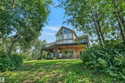 Contemporary architecture featuring a large upper-level deck, expansive windows, a lower-level patio, and a sloped grassy yard surrounded by mature trees - 