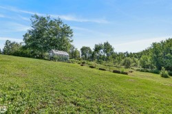 Expansive green space featuring a glass greenhouse, surrounded by mature trees and natural landscaping - 