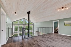 Loft area featuring vaulted ceilings with wood-finish paneling, dark wood-finish flooring, and a black wrought-iron railing - 