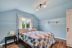Upstairs Bedroom featuring vaulted ceilings, wood-finish flooring, and a window with white curtains - 