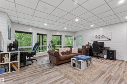 Spacious basement living room featuring wood-finish flooring, white shiplap walls, recessed lighting, and multiple large windows - 