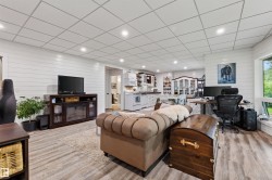 Open-concept living area featuring wood-finish flooring, white shiplap walls, recessed ceiling lighting, and a kitchen area with white appliances - 