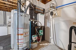 Utility space featuring a water heater, hydronic heating system, exposed ceiling joists, and concrete flooring - 