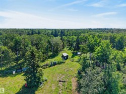 Expansive wooded acreage featuring a cleared grassy area and multiple outbuildings - 