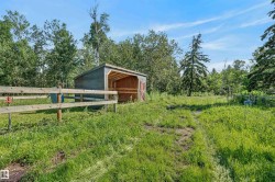 Open-sided shelter with a sloped roof, situated within a fenced grassy area - 
