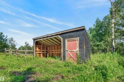 Rustic outbuilding featuring a spacious open-air covered structure with wooden framing, metal roofing, and a solid wood entry door - 