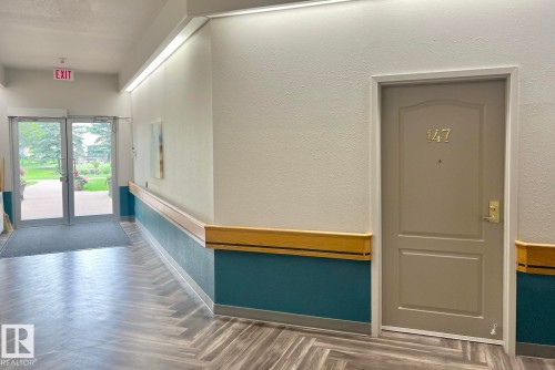 Hallway featuring wood-finish flooring in a herringbone pattern, two-tone painted walls with a wood-finish handrail, and recessed lighting - #147 13441 127 St Nw, Edmonton, AB 