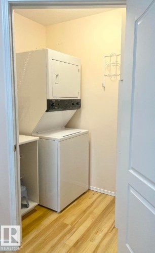 Dedicated laundry area featuring a stacked washer and dryer, wood-finish flooring, and light-toned walls - #147 13441 127 St Nw, Edmonton, AB 