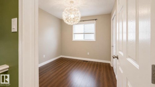 Room featuring wood-finish flooring, a window with horizontal blinds, a decorative overhead light fixture, beige walls, and white trim - 29 Campbell Road, Leduc, AB - Indoor Photo Showing Other Room