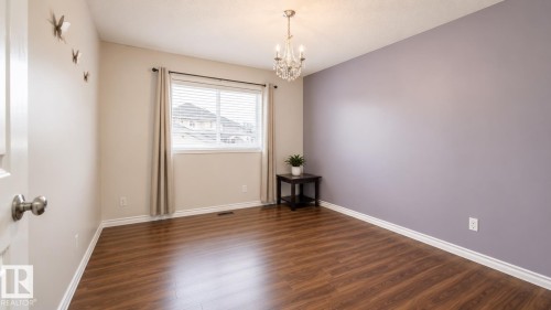 Spacious room featuring wood-finish flooring, a window with blinds and drapes, a crystal chandelier, a two-tone painted wall, and white trim - 29 Campbell Road, Leduc, AB - Indoor Photo Showing Other Room
