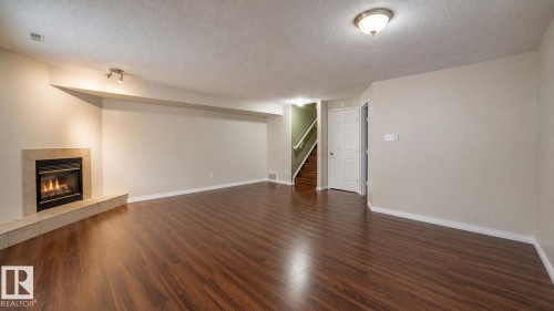 Spacious lower-level area featuring dark wood-finish flooring, a corner fireplace with a light-toned surround, recessed lighting, and a neutral wall palette - 29 Campbell Road, Leduc, AB - Indoor With Fireplace