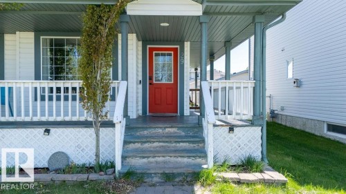 Covered front porch with a vibrant red entry door featuring glass panels - 29 Campbell Road, Leduc, AB - Outdoor