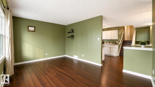 Expansive interior space featuring rich wood-finish flooring, a contemporary accent wall, and bright white baseboards - 29 Campbell Road, Leduc, AB - Indoor