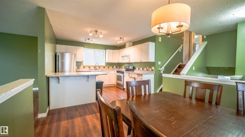 Kitchen and dining area featuring wood-finish flooring, white cabinetry, stainless steel appliances, and a breakfast bar - 29 Campbell Road, Leduc, AB - Indoor Photo Showing Other Room