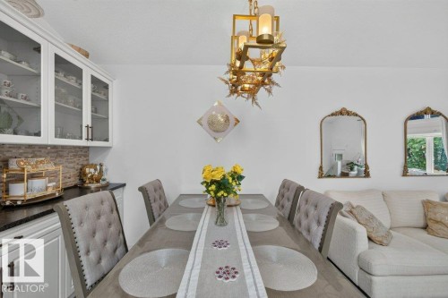 Dining area featuring a rectangular table with six upholstered chairs, a contemporary chandelier, and a built-in buffet with glass-front upper cabinetry and a tiled backsplash - 12219 89 Street Nw, Edmonton, AB - Indoor Photo Showing Dining Room