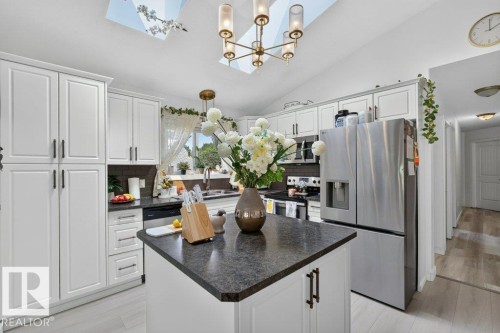 Kitchen featuring a central island with dark countertop, white cabinetry with dark hardware, stainless steel appliances, and dual skylights - 12219 89 Street Nw, Edmonton, AB - Indoor Photo Showing Kitchen With Double Sink