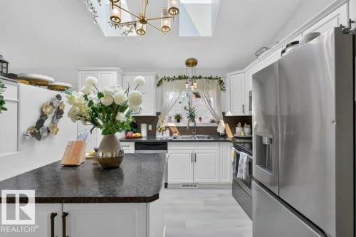 Kitchen featuring white cabinetry, dark countertops, skylights, and stainless steel appliances - 12219 89 Street Nw, Edmonton, AB - Indoor Photo Showing Kitchen With Double Sink