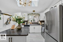 Kitchen featuring white cabinetry, dark countertops, skylights, and stainless steel appliances - 