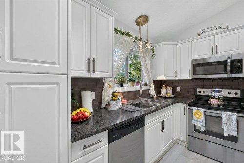 White shaker-style cabinetry with dark hardware, dark countertops, brown subway tile backsplash, and stainless steel appliances - 12219 89 Street Nw, Edmonton, AB - Indoor Photo Showing Kitchen With Double Sink