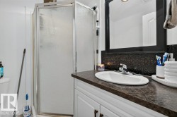 Bathroom featuring a glass-enclosed shower, white vanity cabinetry with dark hardware, a dark patterned backsplash, a countertop with an integrated sink, and a framed mirror - 