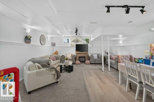 Spacious lower-level area featuring a stone-clad fireplace, carpeted lounge space, and wood-finish flooring - 12219 89 Street Nw, Edmonton, AB - Indoor
