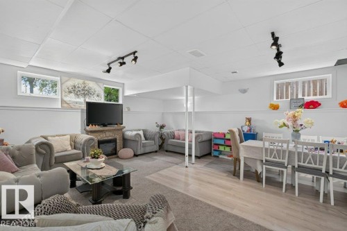 Spacious lower level featuring a stone-clad fireplace, track lighting, wood-finish flooring, and multiple windows - 12219 89 Street Nw, Edmonton, AB - Indoor