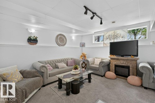Carpeted living area featuring a stone-look fireplace with an electric insert, recessed lighting, and wall-mounted sconces - 12219 89 Street Nw, Edmonton, AB - Indoor Photo Showing Living Room