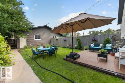 Expansive backyard featuring a wood-finish patio area, perimeter fencing, a concrete pathway, a detached structure with siding, and green lawn space - 12219 89 Street Nw, Edmonton, AB - Outdoor With Deck Patio Veranda