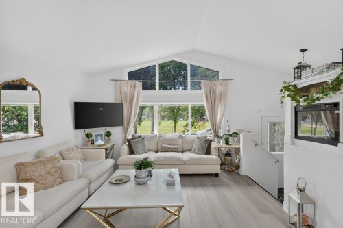 Vaulted ceiling living area featuring large windows, light wood-finish flooring, a contemporary white and gold coffee table, and a built-in electric fireplace - 12219 89 Street Nw, Edmonton, AB - Indoor Photo Showing Living Room